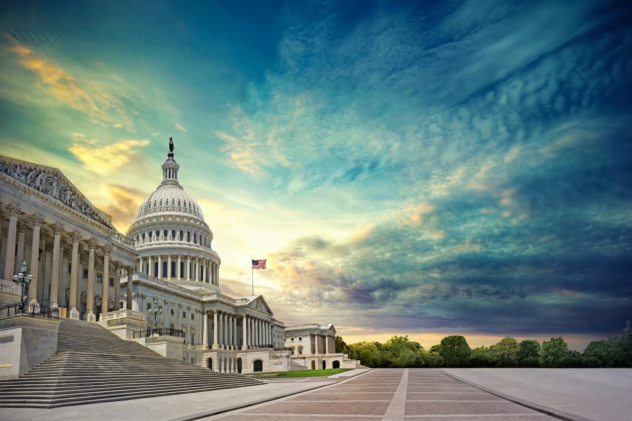The U.S. Capitol building and its dome with an American flag on a flagpole, photographed from the front plaza beneath a colorful cloudy sky