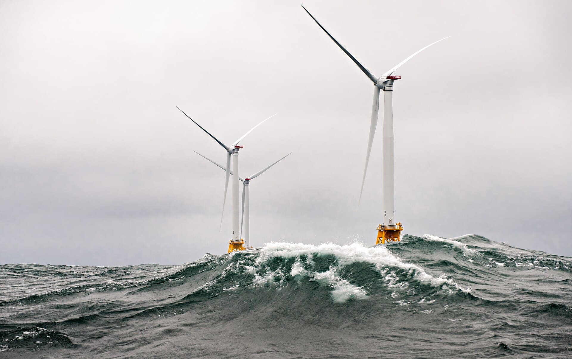 Three offshore wind turbines rising from choppy gray-green seas under an overcast sky